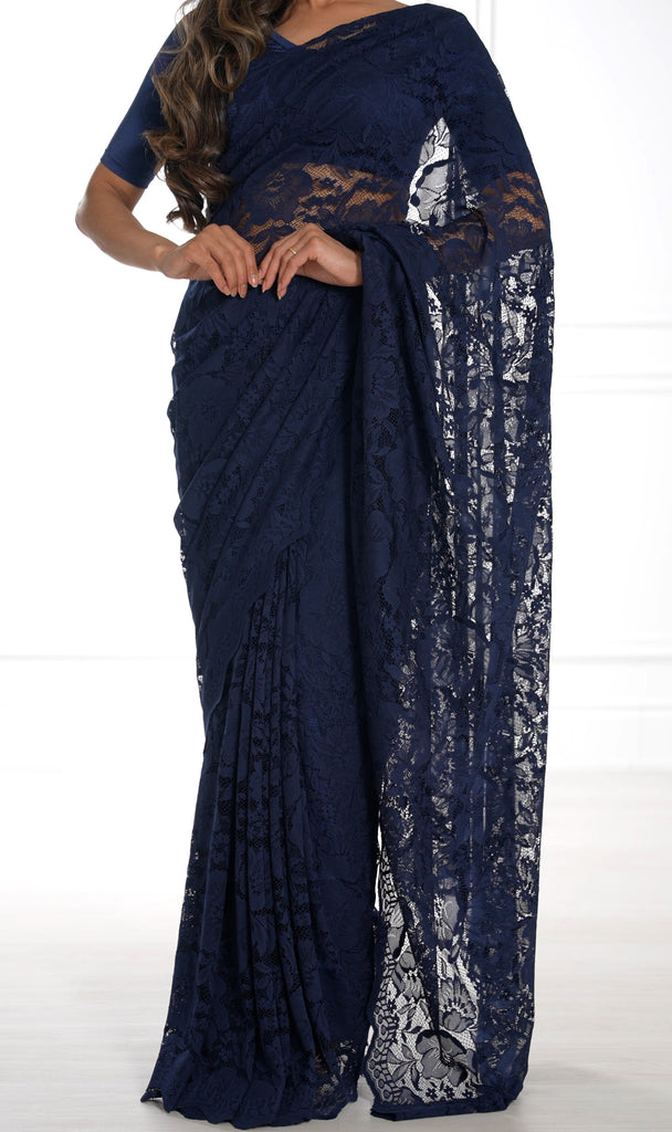 Model draped in a navy blue lace saree with scalloped edging. Model is also wearing a v-neck short sleeve crop top and saree petticoat underneath in matching color.