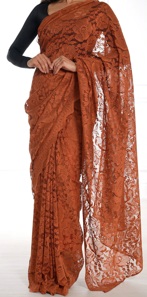 Model draped in a dark orange lace saree with scalloped edging. Model is also wearing a black long sleeve crop top and saree petticoat underneath in matching dark orange color.