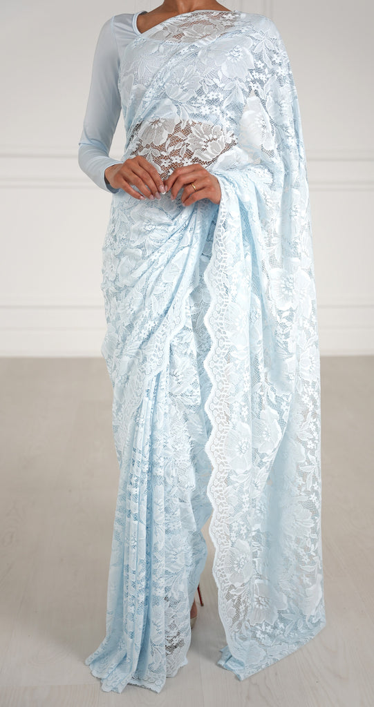 Model draped in a sky blue lace saree with scalloped edging. Model is also wearing a long sleeve crop top and saree petticoat underneath in matching sky blue color.