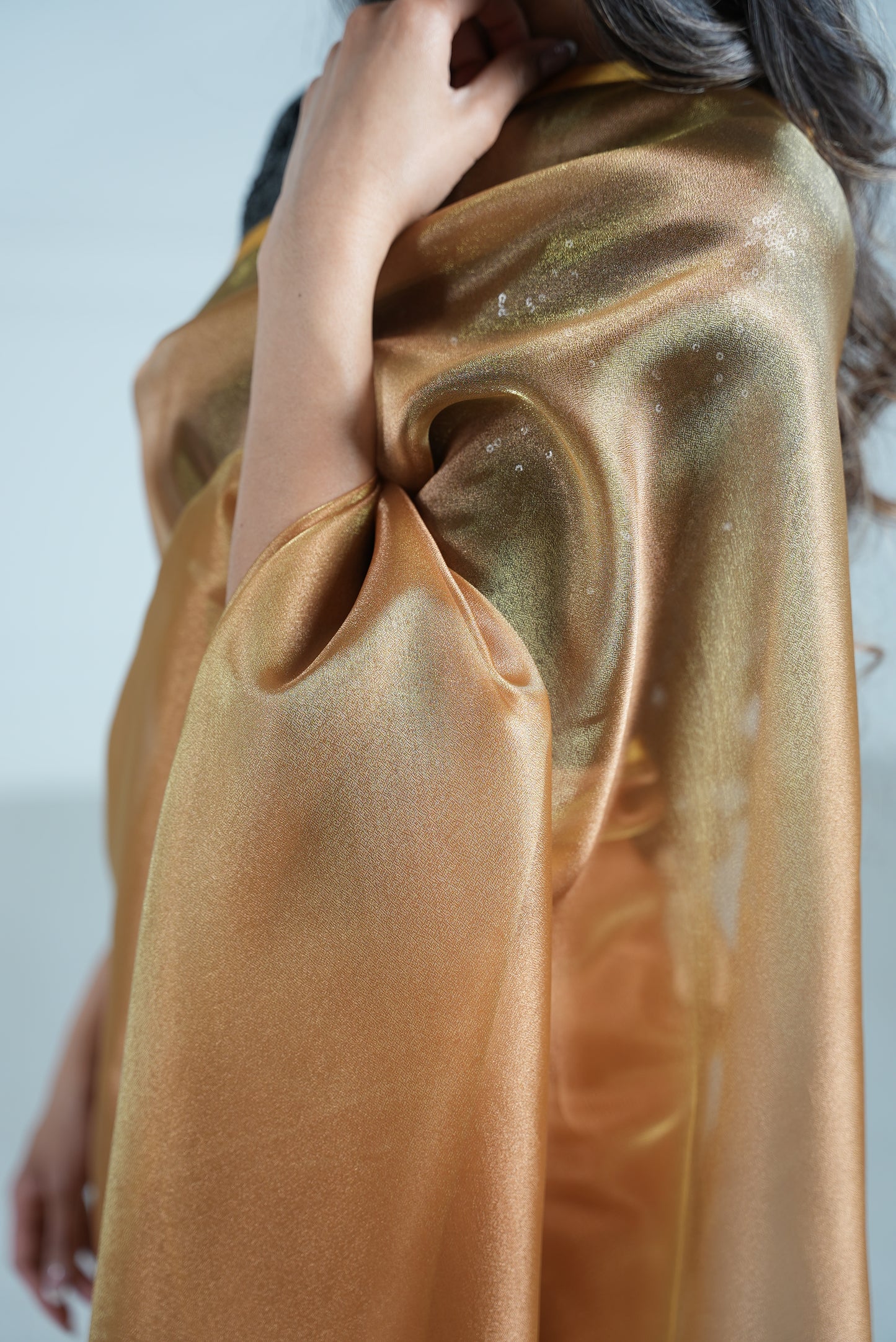 Side close up view of a model draped in a copper organza saree. Model's black 3/4 sleeve sequin crop top also visible underneath.