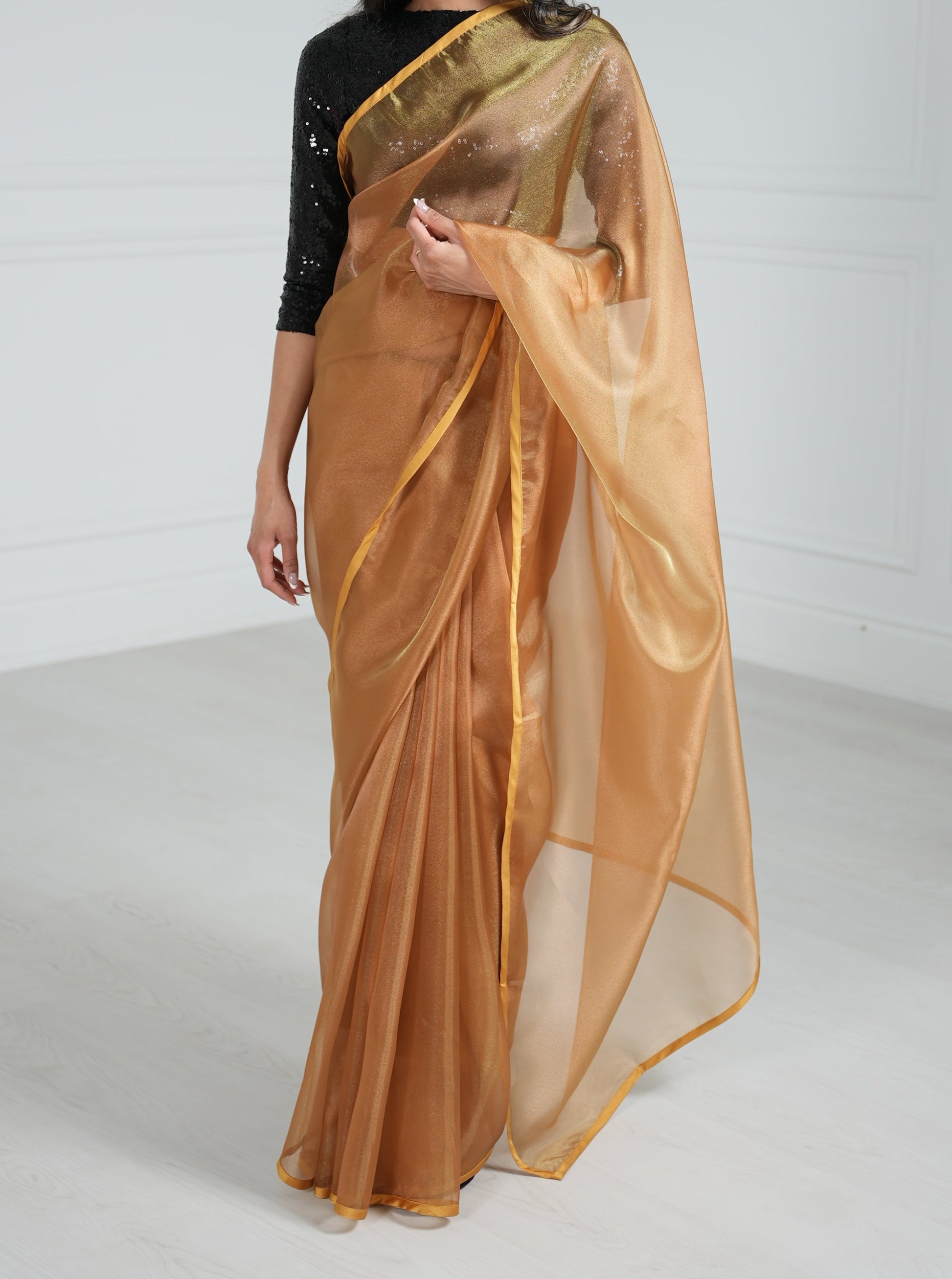 Model draped in a copper organza saree with copper satin border. Model is also wearing a black 3/4 sleeve sequin crop top.