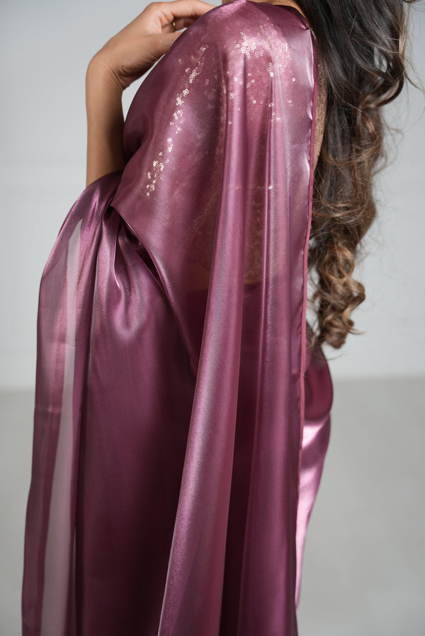 Side view of a model draped in a maroon/burgundy organza saree with maroon/burgundy satin border. Model is also wearing a rose gold 3/4 sleeve sequin crop top.