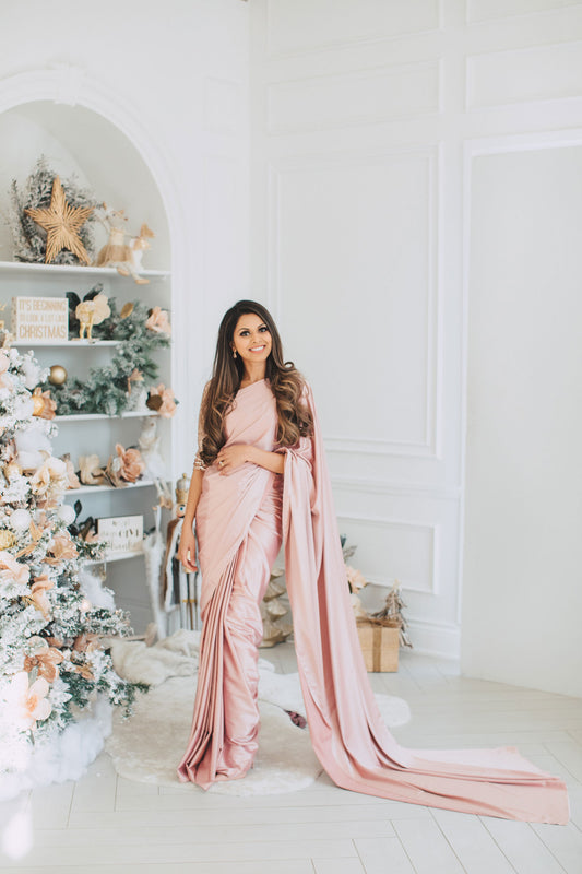 Model wearing a 3/4 sleeve rose gold sequin crop top and draped in a blush pink satin silk saree. Christmas themed background.