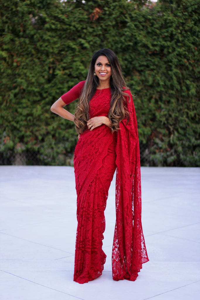 Model draped in a deep red lace saree with scalloped edging. Model is also wearing a short sleeve crop top and saree petticoat underneath in matching color.